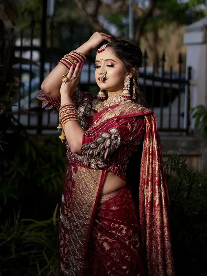 A stunning outdoor shot of a bride in a maroon `Navari` saree. The natural light highlights the glowing skin and the intricate details of her bridal attire.