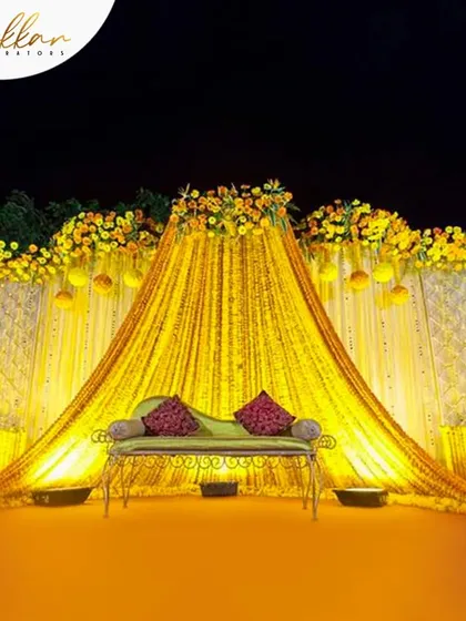 A classic Haldi stage drenched in yellow. The backdrop is created with flowing marigold garlands and drapes, creating a traditional and radiant setting.