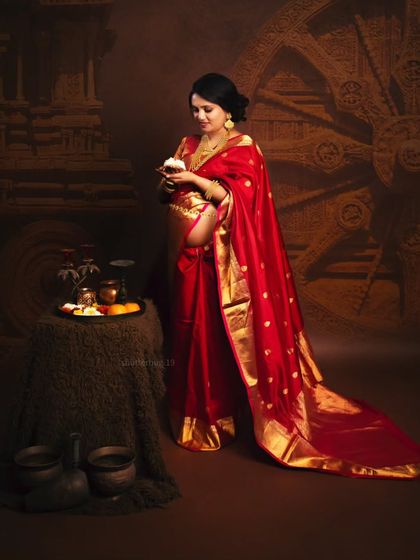 A full portrait of an expecting mother in a traditional red saree, styled with authentic props like a pooja thali and a Konark wheel backdrop. This shoot celebrates the rich cultural roots of the family.