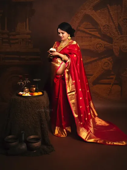 A full portrait of an expecting mother in a traditional red saree, styled with authentic props like a pooja thali and a Konark wheel backdrop. This shoot celebrates the rich cultural roots of the family.