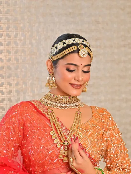 Another shot of this stunning bride, showing her adjusting her heavy necklace. The makeup is kept soft and glowing to balance the ornate jewelry and outfit.