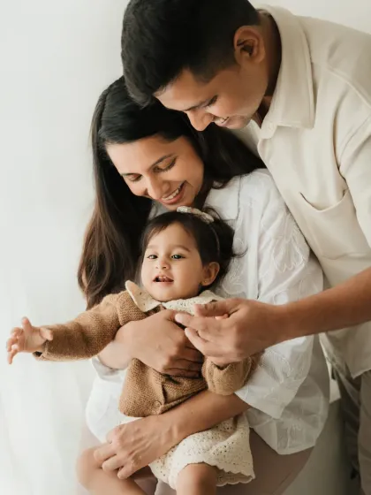 A family of three shares a cuddle. The parents' smiles and the baby's happy expression make this a heartwarming lifestyle shot.