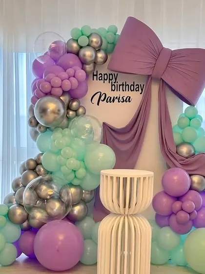 We're always up on the latest trends, like this giant bow decor. A large purple bow drapes over a custom backdrop surrounded by a pastel purple and mint green balloon garland for Parisa's birthday.