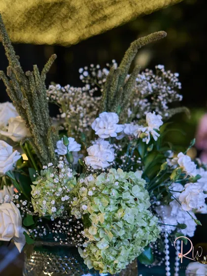 A close-up of a floral arrangement from a Sangeet night, showing the mix of green hydrangeas, white carnations, and delicate pearls.
