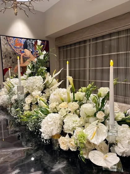 An elegant dining table with a massive runner of white hydrangeas, lilies, and roses, lit by glowing candles.