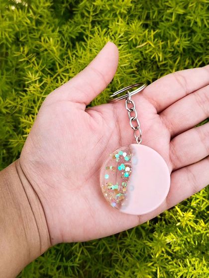 A closer look at the pastel pink and glitter keychain, held in hand to show its size. The combination of opaque color and sparkling clear resin gives it a unique look.