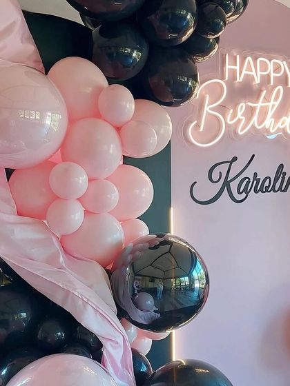 A close-up of the pink and black balloon garland, showing the mix of glossy and matte balloons and the personalized neon sign.