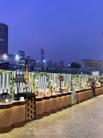 A wide-angle view of our outdoor buffet against the twilight cityscape. The illuminated counters and artistic decor pieces create a dramatic and impressive culinary landscape for your guests to explore.