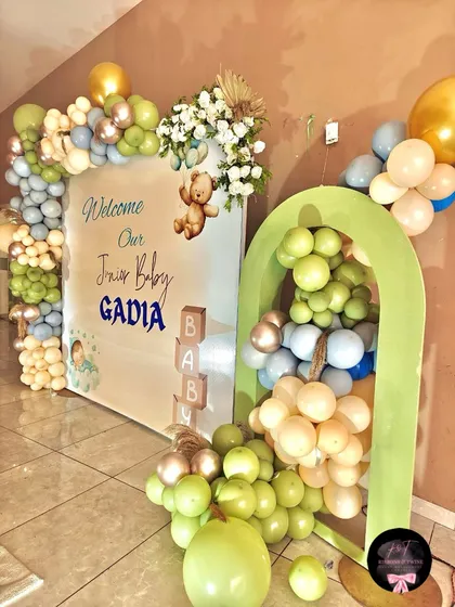 A closer look at the main backdrop, featuring the green arch, floral accents, and personalized 'Welcome Our Junior Baby' signage.