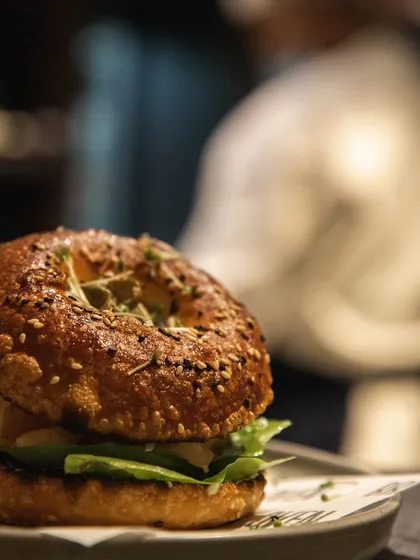 A close-up of our sourdough bagel sandwich, with a soft focus on the bustling cafe vibe in the background.