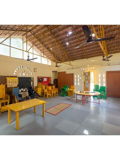 The bright and airy interior of the Spastic Society classroom. The high, vaulted ceiling with its exposed thatch and yellow-painted trusses creates a cheerful and spacious learning environment.