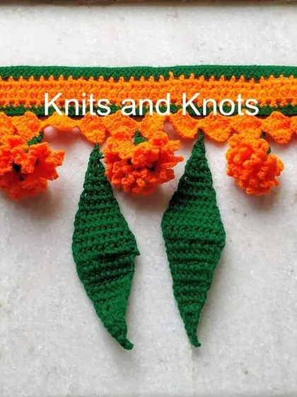 A close up of the orange marigold toran, showing the texture of the crocheted flowers and leaves.