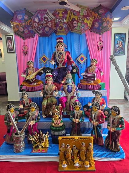 A full view of the colorful Golu doll display against a pink and blue draped backdrop.