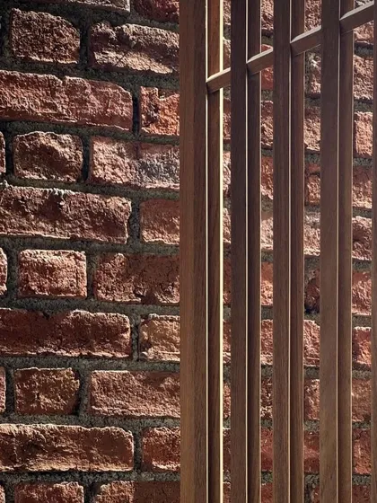A close-up view of the textures of the Kamshet farmhouse. The rough, handmade quality of the brick wall contrasts beautifully with the smooth, precise lines of the timber screen.