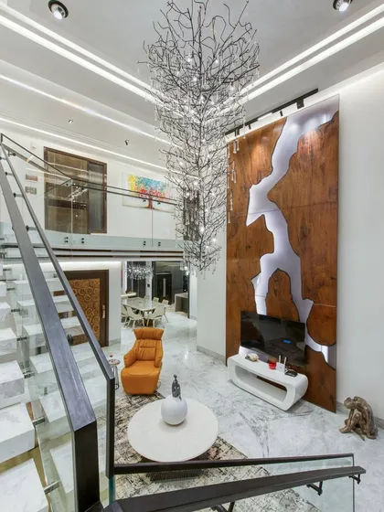 A view from the upper level of the Gallery House, looking down at the living area. The custom wood and resin feature wall and the tree-like chandelier serve as focal points in this double-height space.