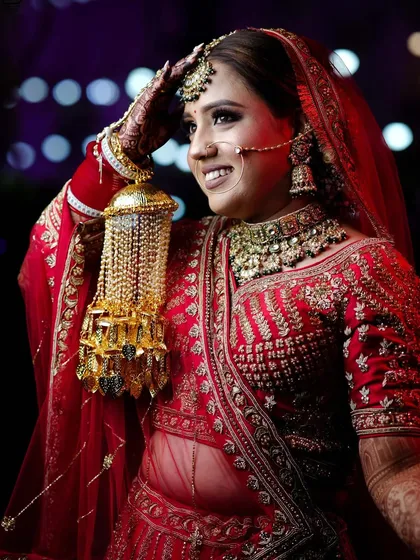A classic bridal pose, with the bride adjusting her 'maang tikka', looking radiant and happy.