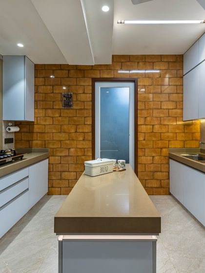 This contemporary kitchen from the Filigree House project features an industrial-inspired brick wall. The light blue cabinets and beige island countertop create a modern palette that is both stylish and functional.