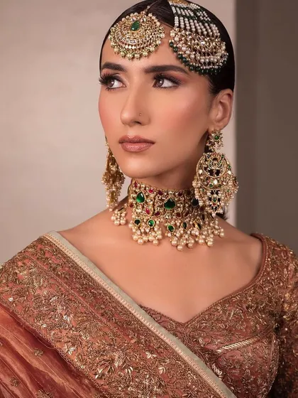A close-up of a traditional bridal look with a modern passa. The makeup is kept clean and elegant, with a focus on the eyes and a soft, neutral lip.