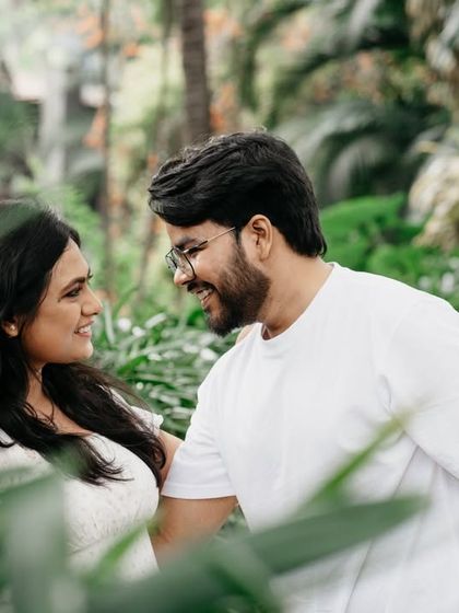 A sweet, candid moment between a couple surrounded by nature. The soft focus on the foreground leaves draws the viewer's eye directly to their happy interaction.