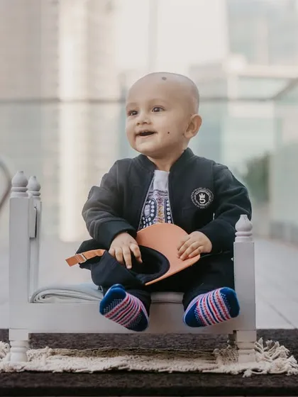 A happy baby enjoying his photoshoot by the pool, sitting on a miniature bed prop with a city skyline in the background.