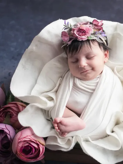 The same sweet girl, now peacefully asleep. This photo showcases the classic, serene newborn portrait, with the baby looking angelic and content, surrounded by soft flowers.