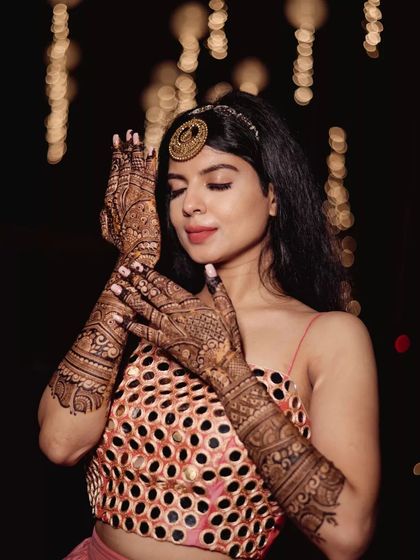 Each bride is stunning in her own way. Here, a classy bride poses elegantly, showcasing her detailed mehendi against a backdrop of festive lights.