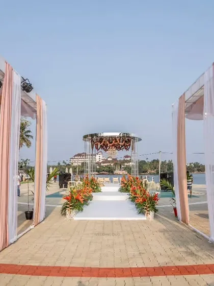 The grand aisle for a waterside wedding, framed by elegant draped structures. The path leads to a modern, circular mandap, creating a sense of symmetry and grandeur.