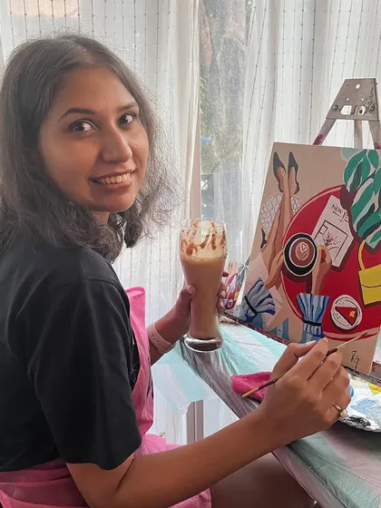 A smiling painter with her coffee themed artwork and a matching cold coffee. The themes of my workshops often tie into the cafe setting.