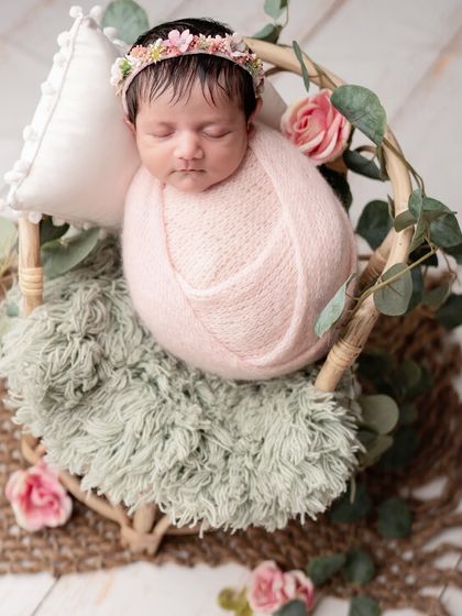 A newborn peacefully sleeping in a beautiful rattan basket, adorned with soft pink roses and eucalyptus.
