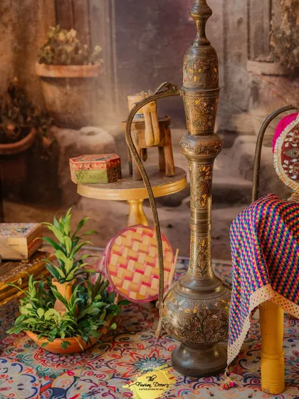 More traditional decor elements, including an ornate brass surahi (water jug) and colourful hand fans, set against a backdrop that evokes the feeling of a Punjabi courtyard.