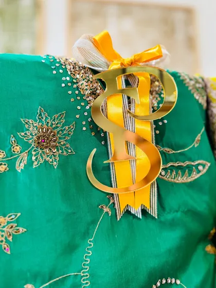 A close-up of the golden initials and yellow ribbon, highlighting the fine embroidery on the emerald green fabric.