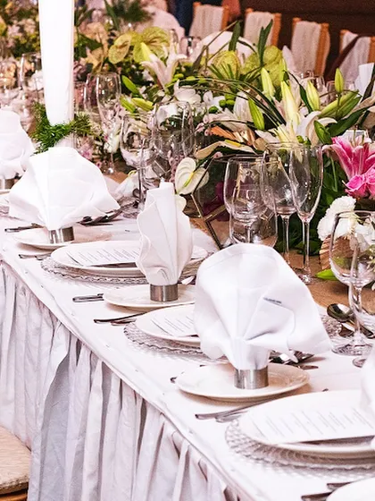 An elegant table setting with crisp white linens, pleated table skirts, and lush floral arrangements. This classic and timeless look is perfect for formal dinners and wedding receptions.