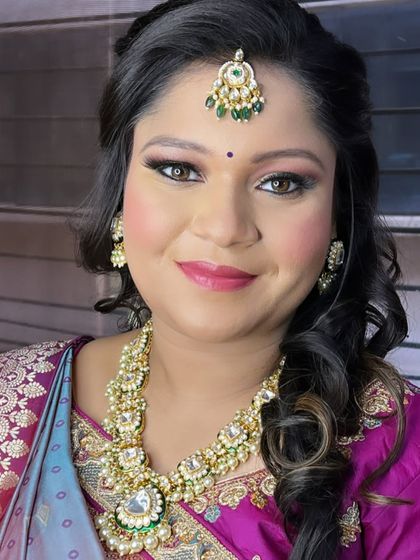 This client looks beautiful in a rented kundan and pearl necklace set with green stone accents, paired with a purple and blue saree for a festive occasion.