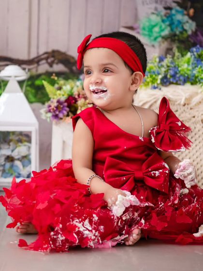 A little lady in red enjoying her cake. The vibrant color of her dress and the messy frosting create a fun and festive first birthday portrait.