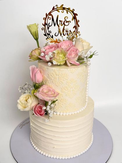 A floral dream turned into a wedding masterpiece. This two-tiered cake combines a rustic textured buttercream finish on the bottom with an elegant stencil pattern on top, all brought together with a beautiful arrangement of fresh pastel roses.