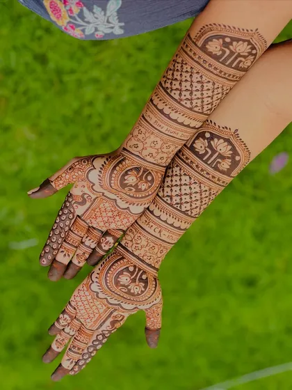 A beautiful outdoor shot showcasing a full bridal design with personalized elements. The natural light brings out the fresh henna paste's texture and detail.