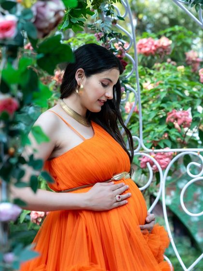 A tender close-up of a mom-to-be in an orange gown, gently cradling her baby bump. The surrounding flowers create a soft, romantic frame for this portrait.