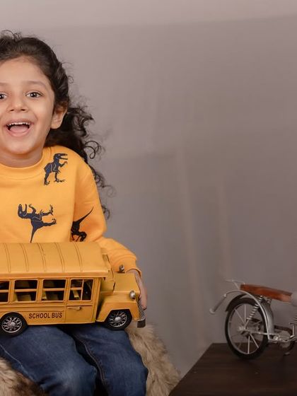 The pure excitement of a child with a new toy. This candid shot captures a boy's joyful expression as he holds up a toy school bus during his studio session.