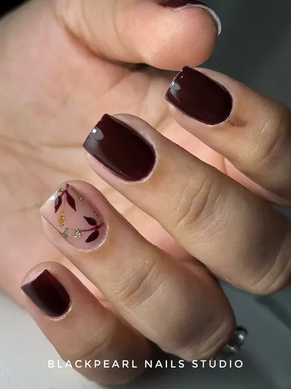 A subtle and luxurious design on short nails. This set features a dark brown polish with a nude accent nail, adorned with delicate, hand-painted leaves and a touch of glitter for an elegant finish.