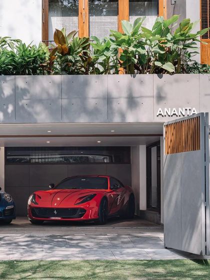 The entrance to 'Ananta' showcases a love for cars, with a bright red Ferrari parked in a clean, modern carport that is integrated into the home's design.
