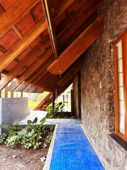 The veranda of the Alibaug residence, almost ready for handover. The space is defined by the rhythm of exposed wooden roof beams and the texture of the local stone, creating a sheltered space that remains open to the elements.