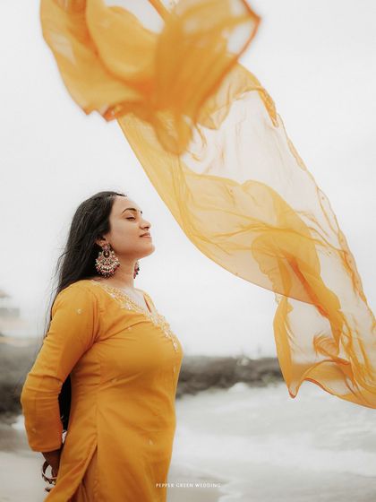 A portrait of the bride-to-be with her yellow dupatta flowing in the wind, creating a sense of freedom and grace during her beach pre-wedding session.