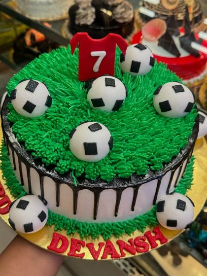 A football-themed cake perfect for a fan's birthday. The green grass piping, fondant footballs, and a jersey with the number 7 make it a winning choice for any soccer lover.