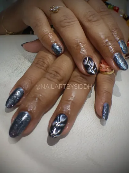A dark, glittery cat-eye polish with a silver leaf-like design on the accent nail for a touch of mystery.