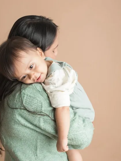 A quiet cuddle on mom's shoulder. This tender portrait captures the feeling of safety and comfort a child finds in their mother's arms.