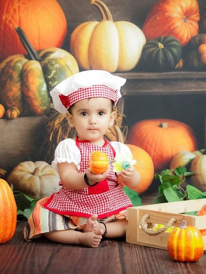 A wider shot of our little chef, surrounded by a harvest of pumpkins and gourds. The details in the background complete the autumn theme.