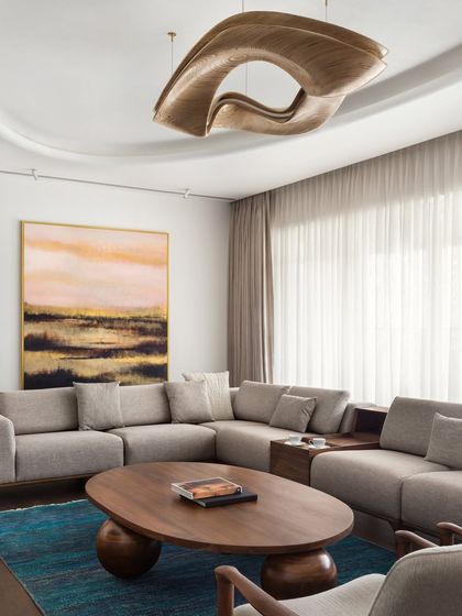 A detail shot of the living room in the West Coast Residence, focusing on the interplay between the curved wooden coffee table, the soft sofa, and the abstract painting.