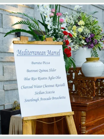 A menu board for our "Mediterranean Marvel" offerings, elegantly displayed on a wooden easel and flanked by floral arrangements, signaling a gourmet experience to come.