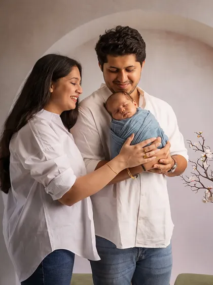 A candid moment of a new family. The mother looks on lovingly as the father holds their sleeping baby, creating a beautiful portrait of shared parenthood.