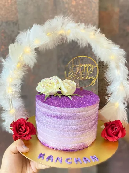 Presenting our signature hoop cake, a total showstopper for any glam celebration. This chocolate cake features a sparkling purple finish, fresh flowers, and a feather hoop with fairy lights, making it a truly Pinterest-worthy centerpiece.